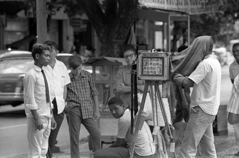 Sou fotógrafo. Sou nordestino. Lá chamam o fotógrafo da praça de lambe lambe. Porque não sei. Todo dia armo a minha caixa fotográfica de madeira no tripé preso em três cabos de vassouras.